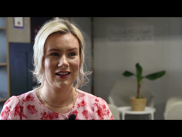 A still from a cyber security video, showing a woman wearing a pink patterned shirt with blonde hair.